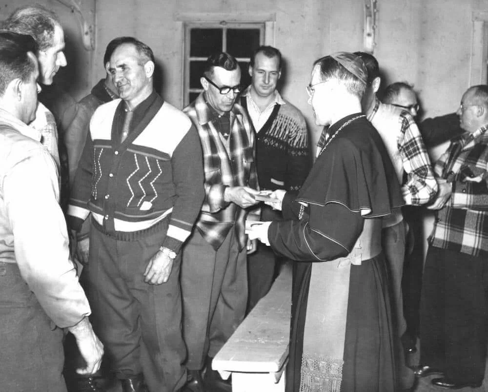Bishop Couturier talks with lumberjacks in the camp
